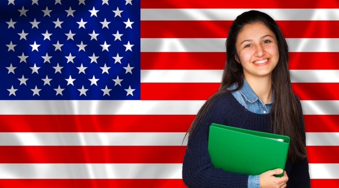 estudante em frente de uma bandeira dos estados unidos. Saiba aqui sobre o valor do visto americano